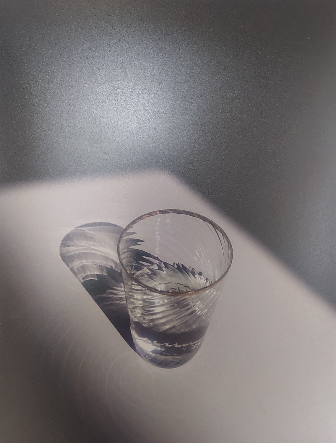 Czarno-białe zdjęcie przedstawiające szklany kieliszek do połowy napełniony przezroczystym płynem.