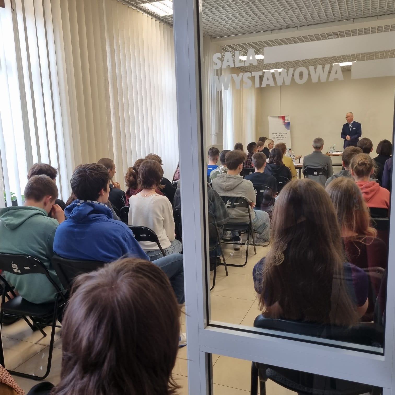 Zdjęcia przedstawiają salę wystawową Biblioteki Pedagogicznej w Toruniu. W sali znajdują się: publiczność, jurorzy, uczestnicy debaty, prowadzący debatę.