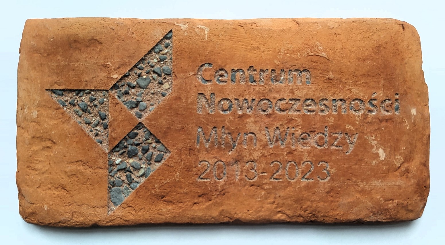 Tabliczka w kształćie cegły z napisem: Centrum Nowoczesności Młyn Wiedzy 2013-2023