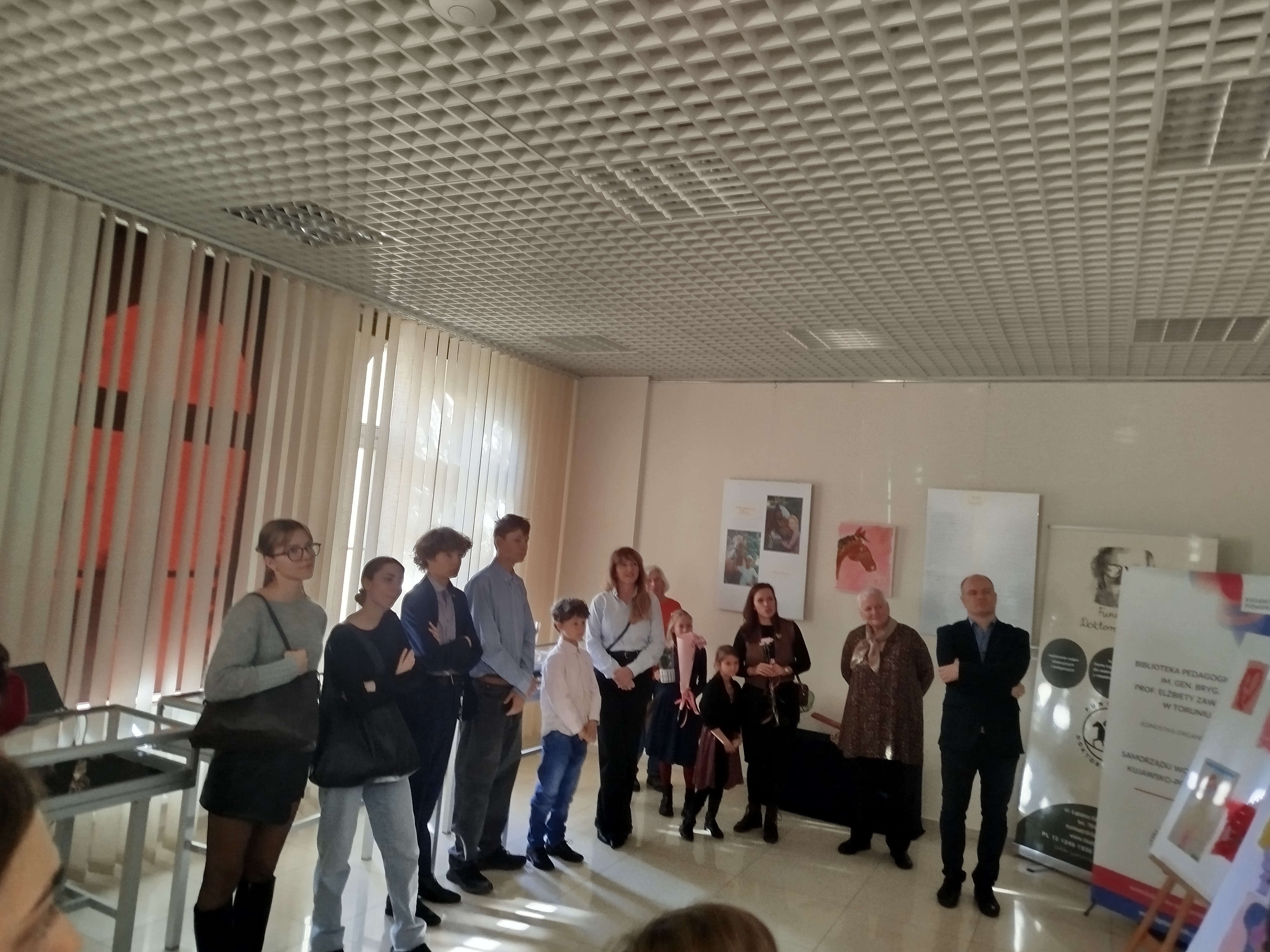 Grupa ludzi stoi w sali wystawowej Biblioteki Pedagogicznej w Toruniu.