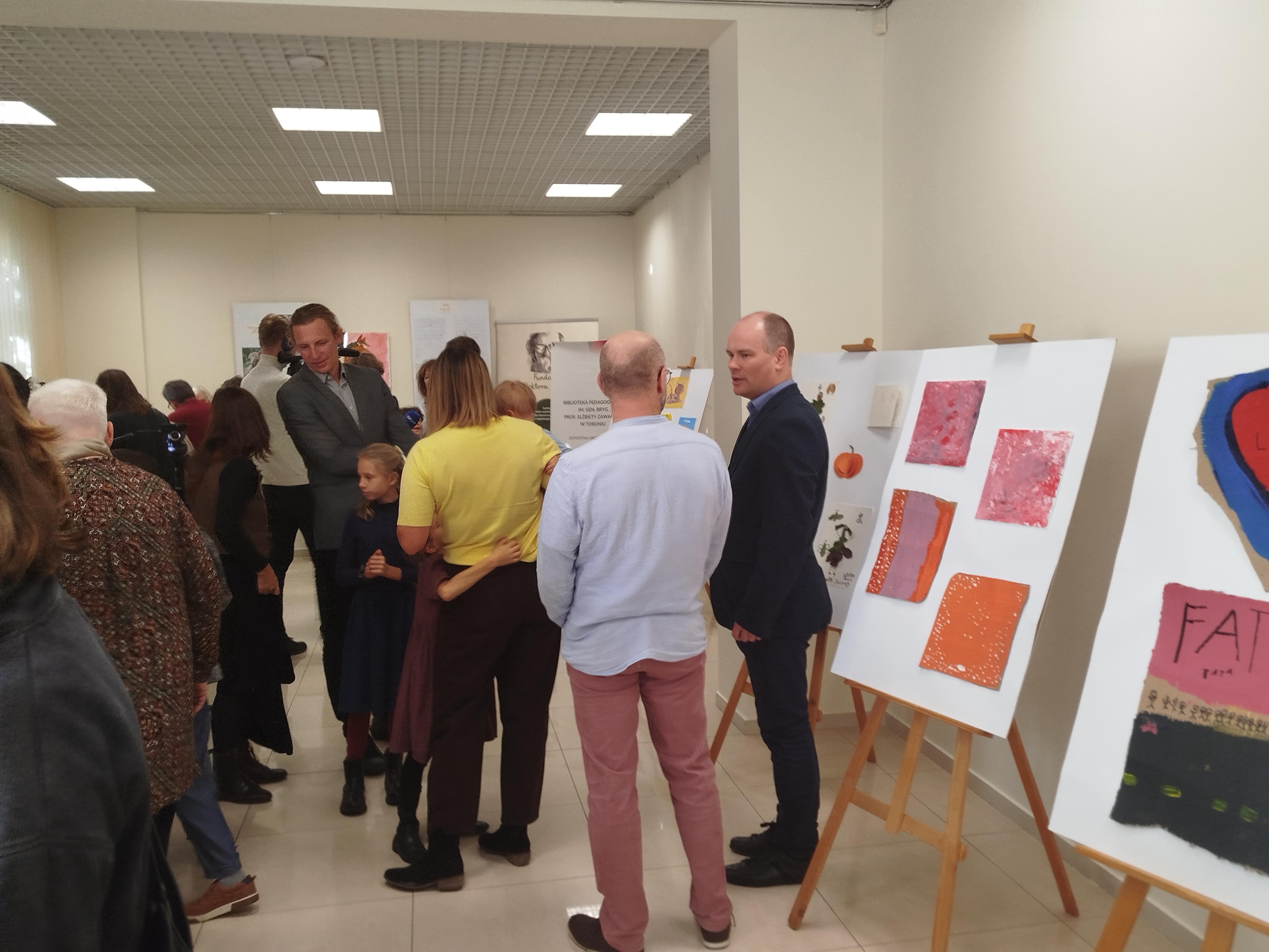 Grupa ludzi stoi w sali wystawowej Biblioteki Pedagogicznej w Toruniu.