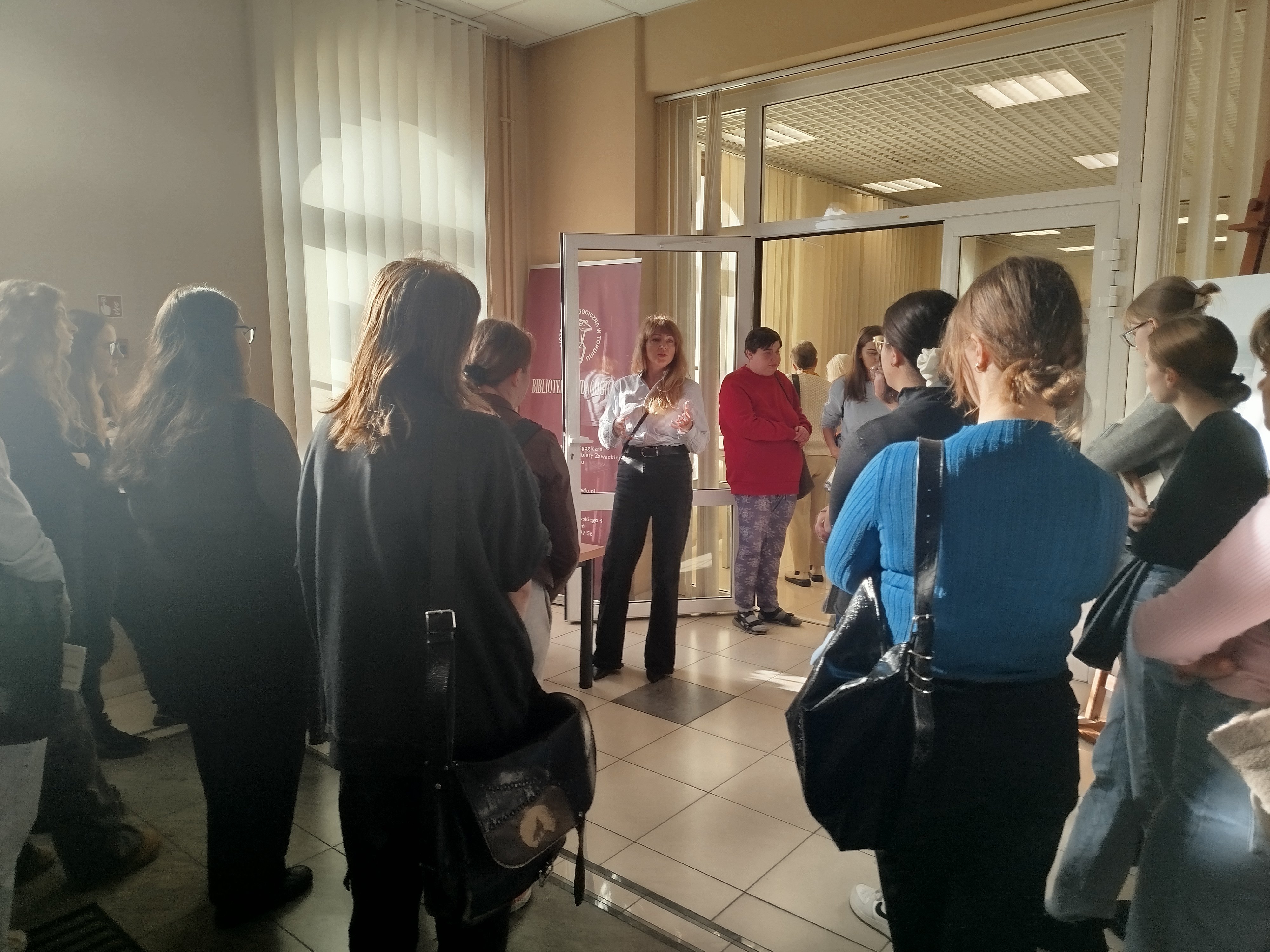 Grupa ludzi stoi w sali wystawowej Biblioteki Pedagogicznej w Toruniu.