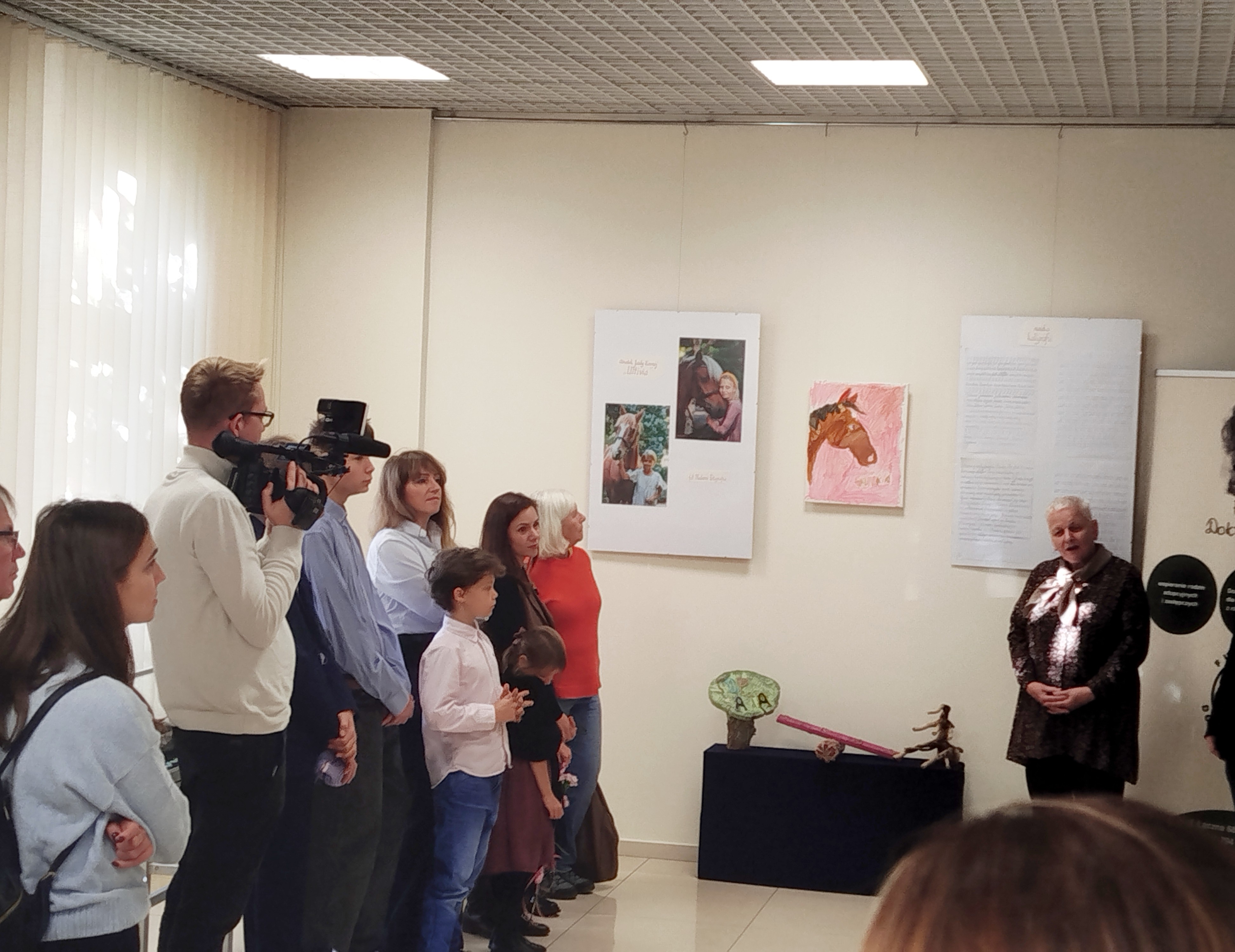 Grupa ludzi stoi w sali wystawowej Biblioteki Pedagogicznej w Toruniu.